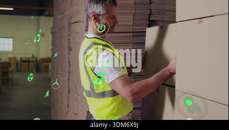 Aligning male worker wearing high-vis vest moving cardboard boxes in storage, with green overlays Stock Photo