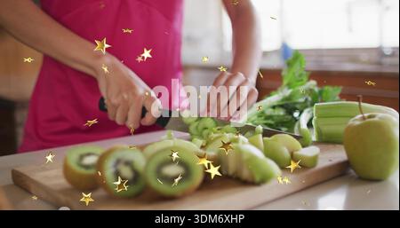 Slicing woman in bright pink top using black-handled knife on kitchen countertop, with kiwis Stock Photo