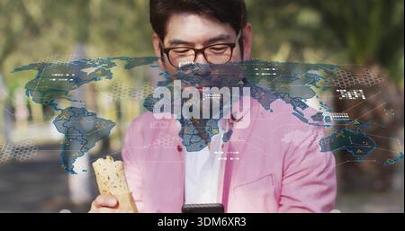 Standing Asian man in pink blazer holding wrap, checking smartphone on park walkway with AR overlay Stock Photo