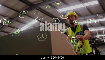 Operating worker in hard hat pushing pallet jack with box in warehouse, AR icons, copy space Stock Photo