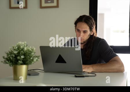 Man working remotely on laptop at home office desk Stock Photo