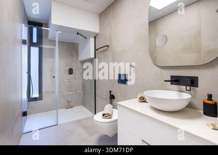 Contemporary bathroom featuring walk-in shower, neutral tiles, vessel sink, and sleek black fixtures Stock Photo