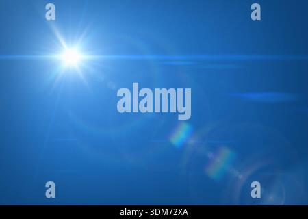 The bright Sun with rays against clear blue sky. Sun flare on blue. Sun is in the upper left corner. There is a sunbeams with natural lens flare. Stock Photo