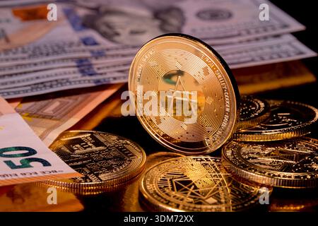 Gold Cardano ADA coin with Bitcoin and EOS alongside euro and US dollar banknotes. Concept of cryptocurrency. Stock Photo