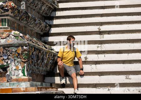 BANGKOK, THAILAND-JAN 15, 2026: Male backpack sitting and and exploring at Thai temple, front view, at Wat Arun. Stock Photo