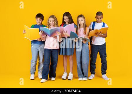 Group of preteen pupils reading books together on yellow studio background Stock Photo