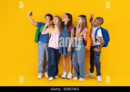 Preteen children taking selfie together on yellow studio background Stock Photo