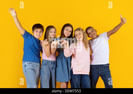 Preteen children smiling and making friendly gestures on bright yellow background Stock Photo