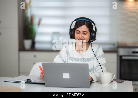 Young adult woman working remotely from home with headset and laptop Stock Photo