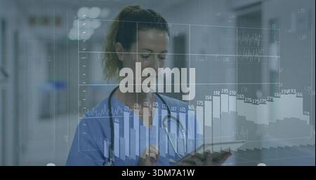 Standing nurse in blue scrubs and stethoscope reviewing tablet in hospital corridor, showing charts Stock Photo