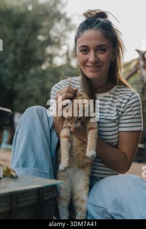 Happy woman holding ginger cat outdoors expressing pet ownership Stock Photo