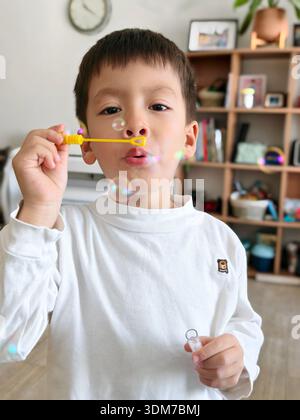 4 year old boy joyfully exudes happiness while blowing bubbles at home, capturing a playful moment of creativity and innocent fun in a cozy and inviti Stock Photo