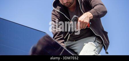 Installer fixing solar panel with a cordless drill on a residential house roof Stock Photo