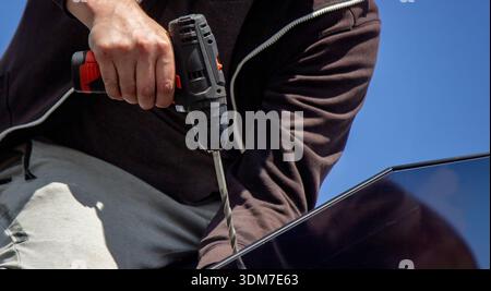 Installer fixing solar panel with a cordless drill on a residential house roof Stock Photo