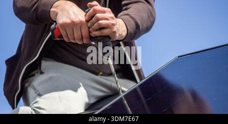 Installer fixing solar panel with a cordless drill on a residential house roof Stock Photo