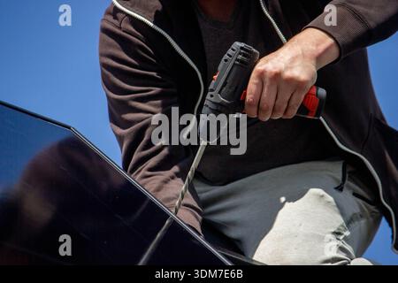 Installer fixing solar panel with a cordless drill on a residential house roof Stock Photo