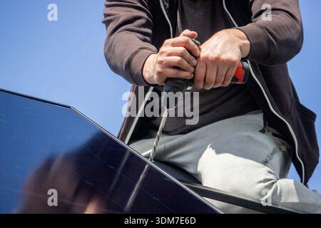 Installer fixing solar panel with a cordless drill on a residential house roof Stock Photo