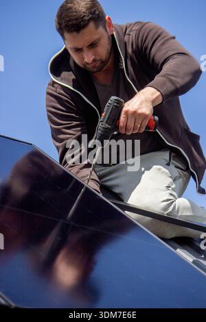Installer fixing solar panel with a cordless drill on a residential house roof Stock Photo