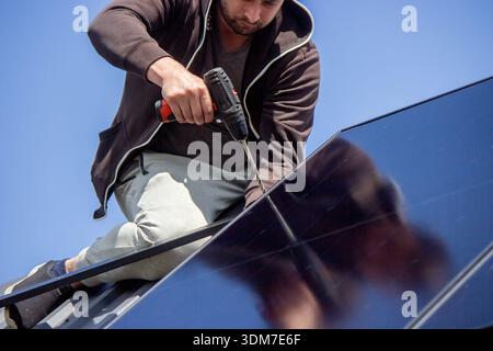 Installer fixing solar panel with a cordless drill on a residential house roof Stock Photo