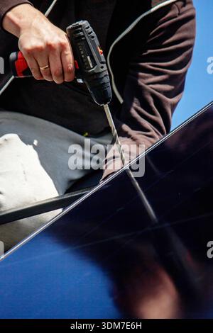 Installer fixing solar panel with a cordless drill on a residential house roof Stock Photo