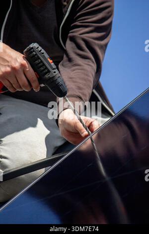 Installer fixing solar panel with a cordless drill on a residential house roof Stock Photo