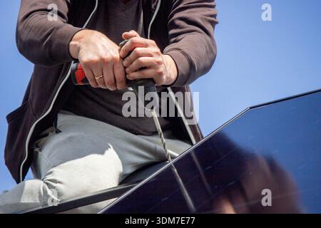 Installer fixing solar panel with a cordless drill on a residential house roof Stock Photo