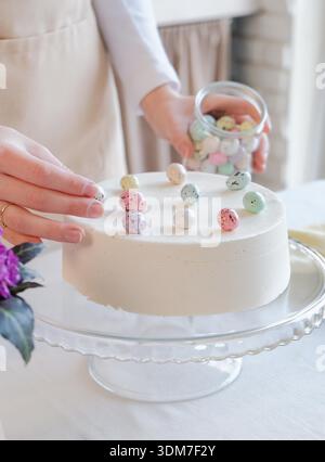 Happy Easter. cropped shot of woman making Easter cake in pastel colors in the kitchen, getting ready for holiday, decorating cake with sweet eggs Stock Photo