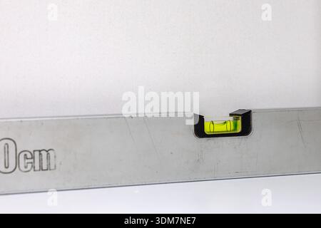 An aluminum spirit level on a yellowed cabinet hanging on a kitchen wall, checking the level and plumbness when hanging kitchen cabinets, a carpenter Stock Photo