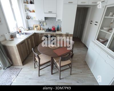 Living room design combined with kitchen, featuring white sideboard. Set of wooden furniture with beech veneer, table, and chairs. Scandinavian-style Stock Photo