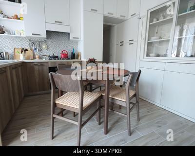 Living room design combined with kitchen, featuring white sideboard. Set of wooden furniture with beech veneer, table, and chairs. Scandinavian-style Stock Photo