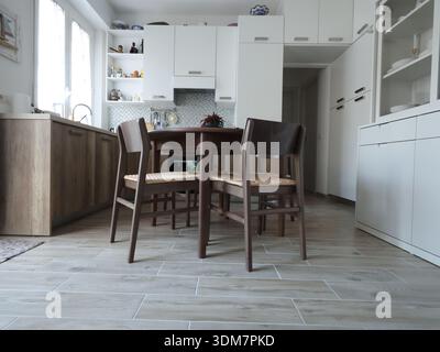 Living room design combined with kitchen, featuring white sideboard. Set of wooden furniture with beech veneer, table, and chairs. View from below Stock Photo