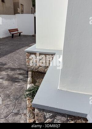 Traditional Cycladic architecture detail in Emporio, Santorini, Greece. Whitewashed walls, stone foundation, and patterned courtyard paving with a lon Stock Photo