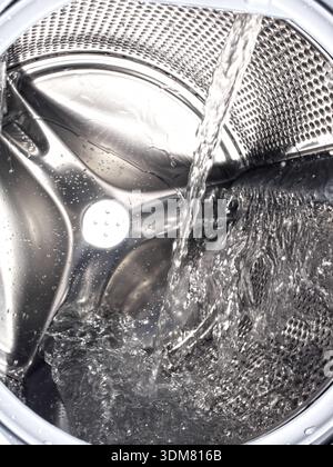 Water pouring into stainless steel washing machine drum Stock Photo