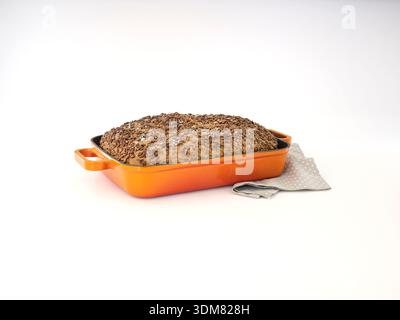 Freshly baked seeded bread loaf in orange baking dish isolated on white Stock Photo