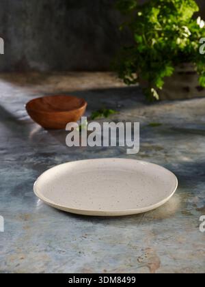 ceramic plate on stone surface with wooden bowl and greenery Stock Photo