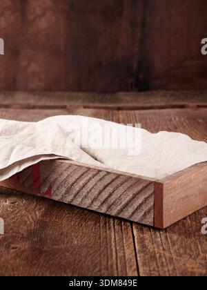 Rustic wooden tray with draped white linen cloth on weathered wood. Stock Photo