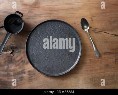 Dark textured ceramic plate on rustic wooden table, top view flat lay Stock Photo