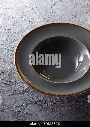 Empty grey ceramic bowl on textured dark grey cracked concrete background, Stock Photo