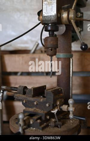 Mississippi, United States – January 20, 2026: Rusted drill press with metal vise mounted on a worktable inside a farm workshop. Stock Photo