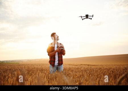Looking at the drone, controlling it. Male farmer is on the wheat agricultural field. Stock Photo