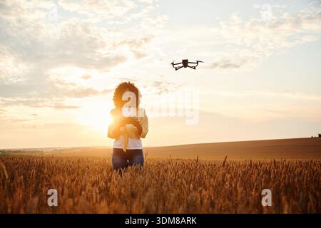 Controlling the drone. Beautiful woman is on the wheat agricultural field. Stock Photo