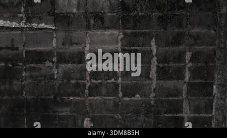 Dark moody weathered concrete block wall with cracked mortar, peeling cement and stains. Grungy urban industrial texture in low light Stock Photo