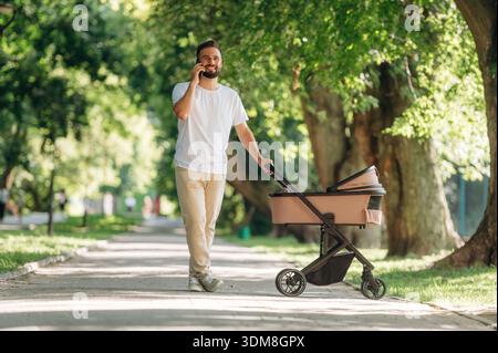 Talking by phone. Father is with cradle, having a walk in the park. Stock Photo
