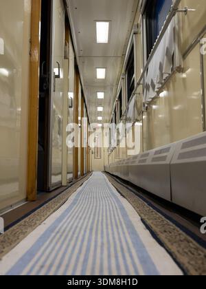 Train journey corridor presenting empty pathway with blue striped runner carpet Stock Photo