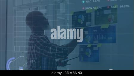 Pointing man in plaid shirt holding tablet reviewing charts, sticky-notes on glass wall, copy space Stock Photo