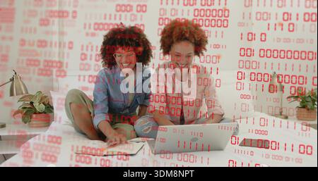 Collaborating women in denim and light shirts using laptop in bedroom, red binary overlay Stock Photo