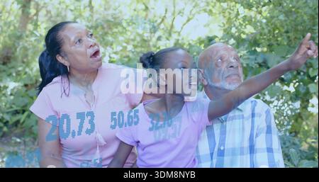 Pointing granddaughter in purple tee sitting between senior couple on park bench with blue overlay Stock Photo