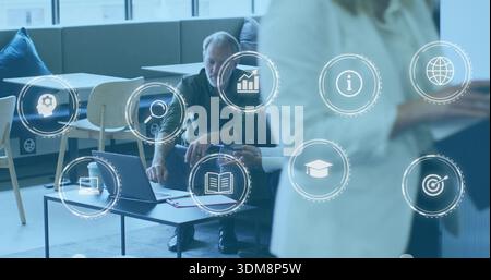 Leaning senior man pointing at open laptop in office lounge, woman in light blazer holding tablet Stock Photo