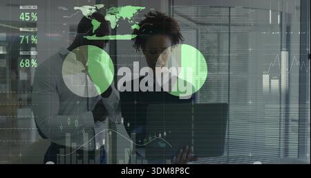Reviewing two professionals in shirt and sweater examining laptop in office with green data overlay Stock Photo