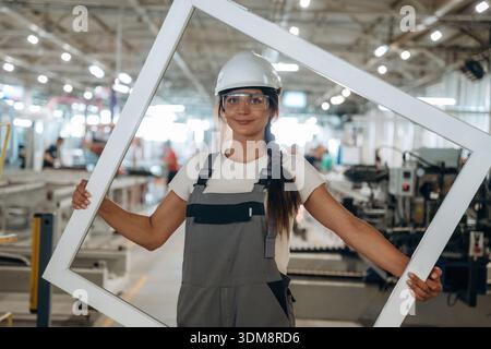 Big frame in hands. Woman is in the window making factory. Stock Photo